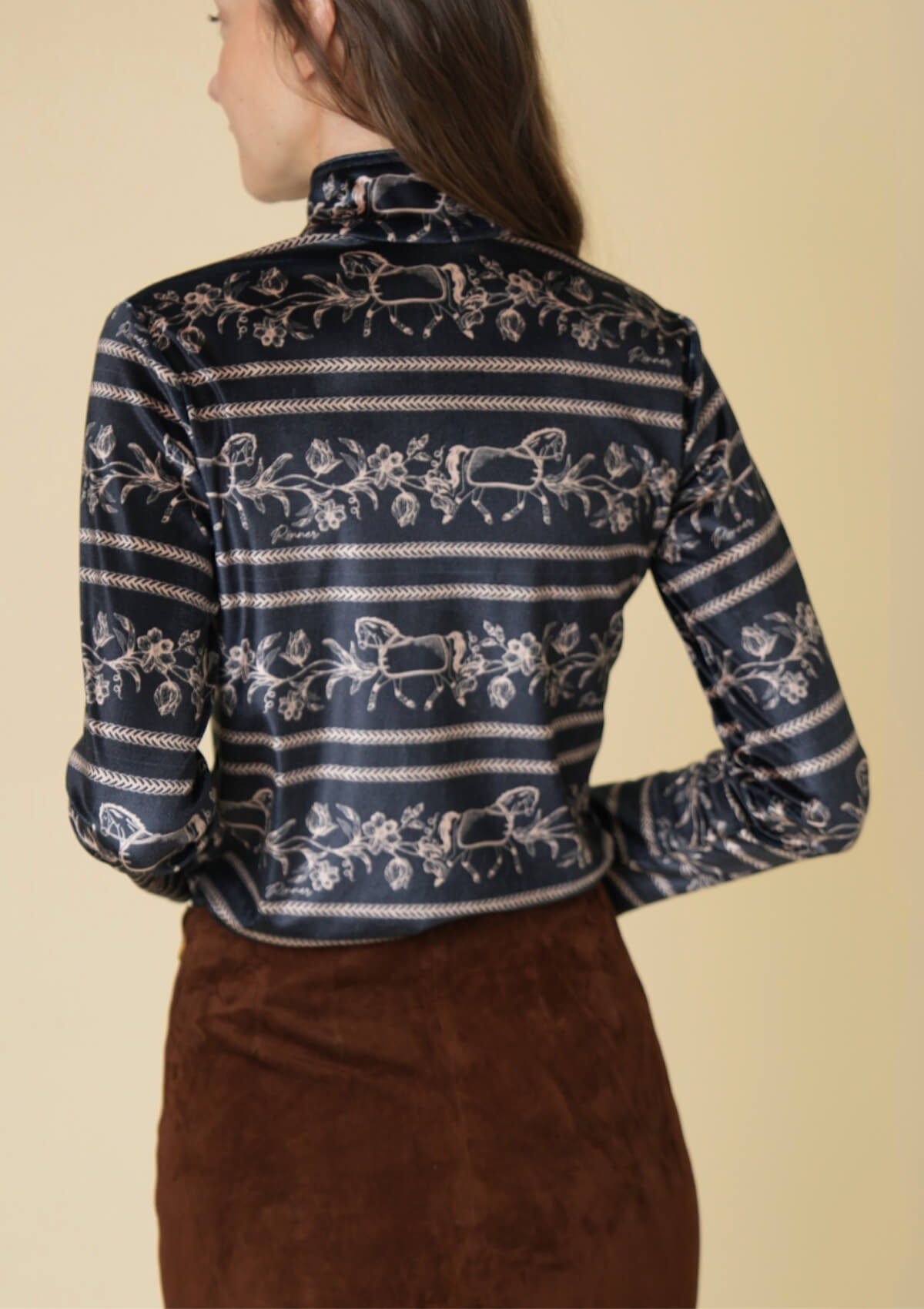 Woman wearing a black patterned shirt with long sleeves against a beige background