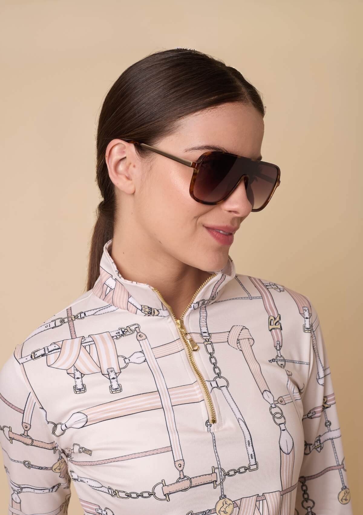 Woman wearing sunglasses and a patterned shirt against a beige background