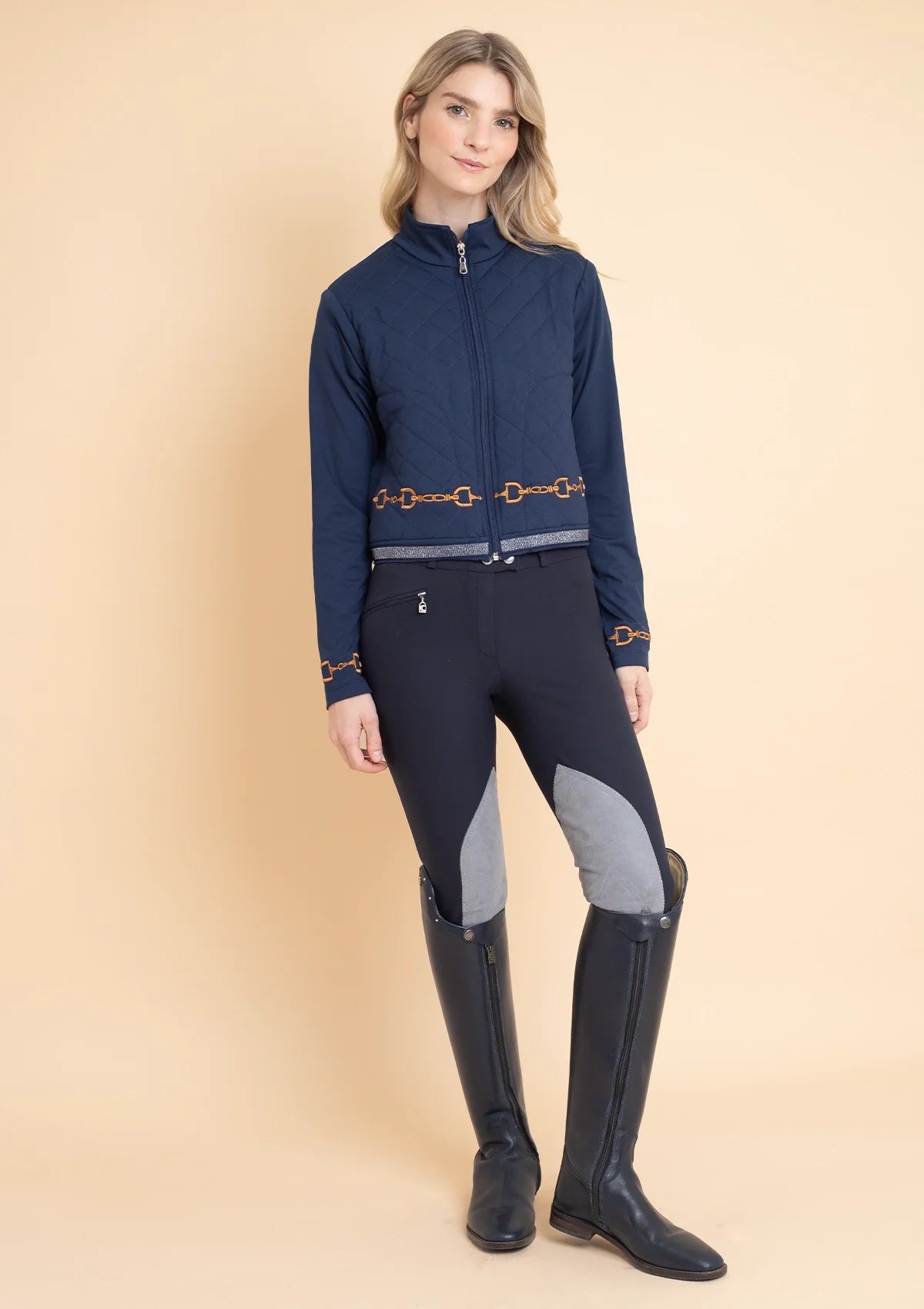 A woman wearing a navy blue equestrian jacket with embroidered details and a high collar, paired with dark riding pants and black boots.